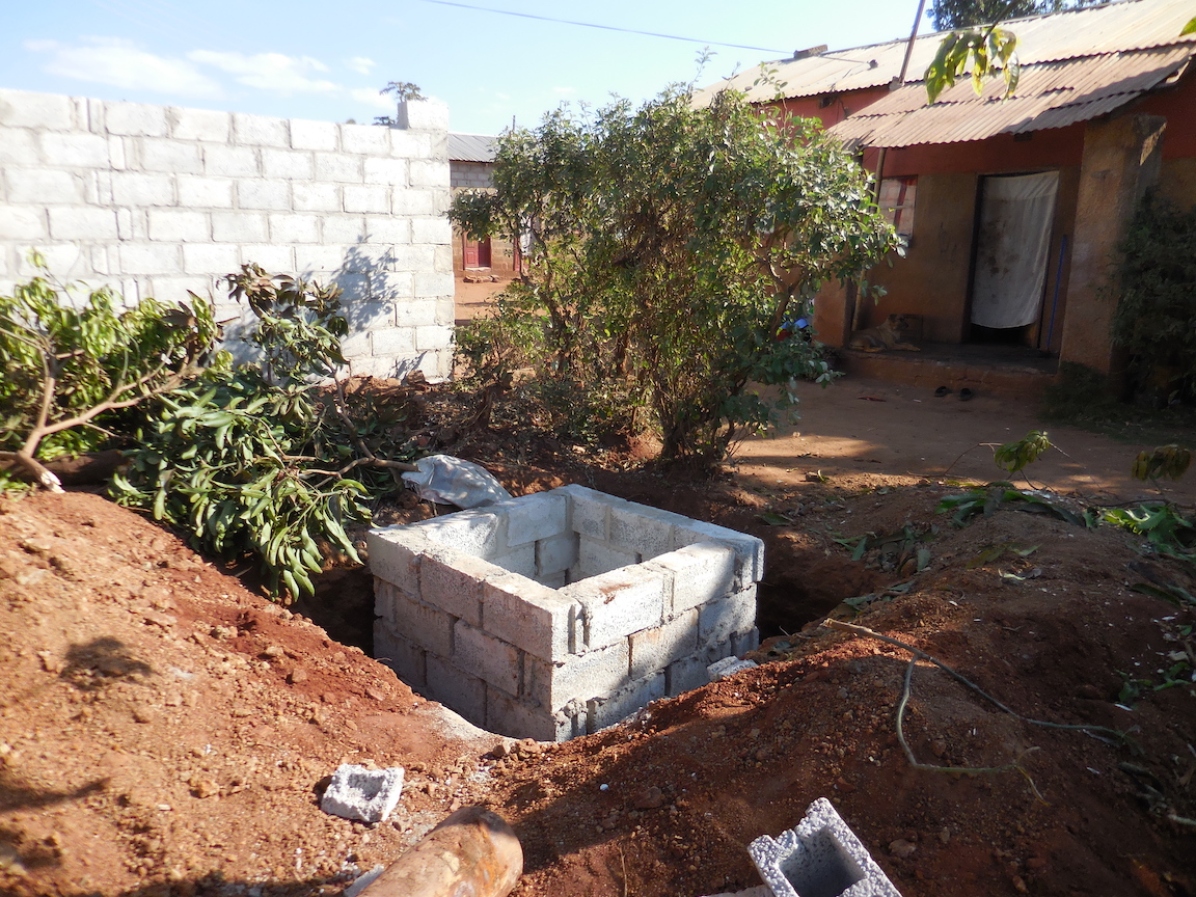 New pit latrine is being constructed. Brenda and her family do not have their own toilet and must walk 3 houses from theirs to use their neighbour's pit latrine. The neighbour's latrine only has pieces of fabric with holes draped around it for privacy.